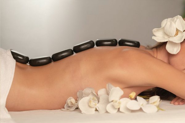 A woman lying on her stomach surrounded with white flowers and with a row of smooth rocks on her spine.